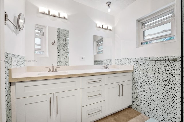 full bath with tiled shower, a sink, tile walls, and double vanity