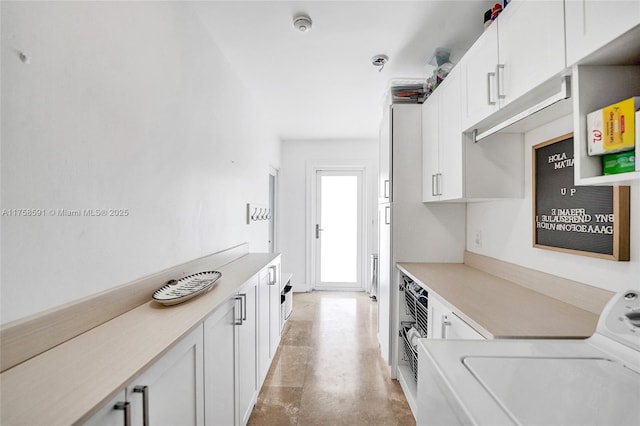 kitchen with finished concrete floors, light countertops, washer / dryer, and white cabinetry