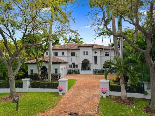 mediterranean / spanish house featuring decorative driveway, a fenced front yard, and stucco siding