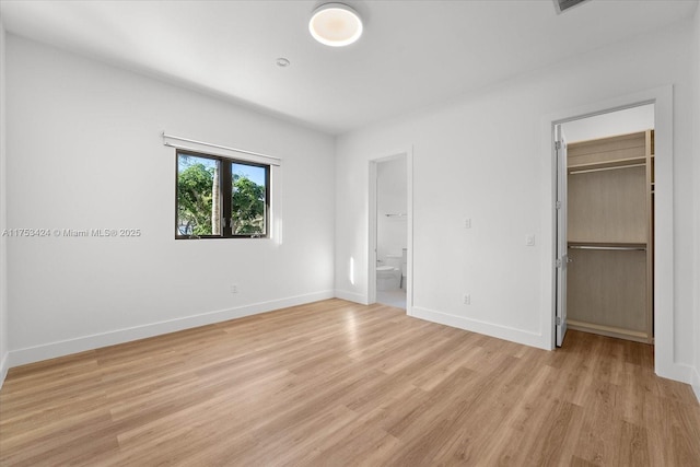 unfurnished bedroom with light wood-type flooring, a closet, connected bathroom, baseboards, and a spacious closet