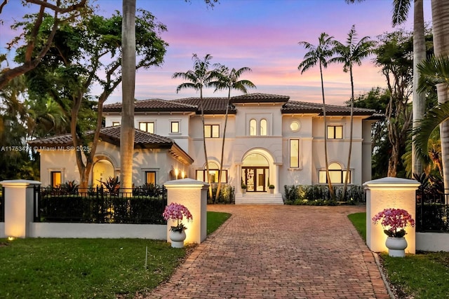 mediterranean / spanish-style home featuring decorative driveway, a tile roof, a fenced front yard, and stucco siding