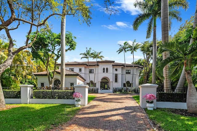 mediterranean / spanish-style home featuring a fenced front yard, stucco siding, a tiled roof, and decorative driveway