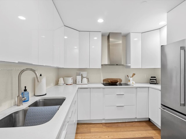 kitchen featuring freestanding refrigerator, a sink, wall chimney exhaust hood, and modern cabinets