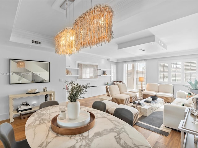 dining area featuring a tray ceiling, light wood-style flooring, visible vents, and crown molding