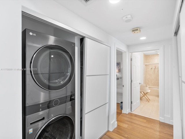 laundry area with stacked washer and clothes dryer, light wood-style flooring, and laundry area