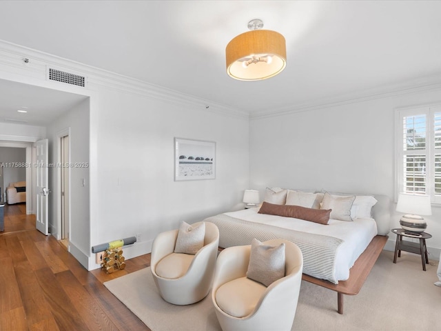 bedroom with baseboards, visible vents, crown molding, and wood finished floors