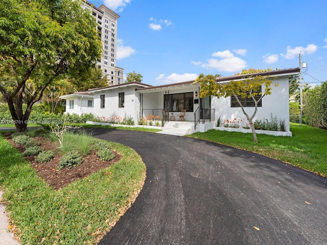 ranch-style home featuring aphalt driveway, stucco siding, and a front lawn