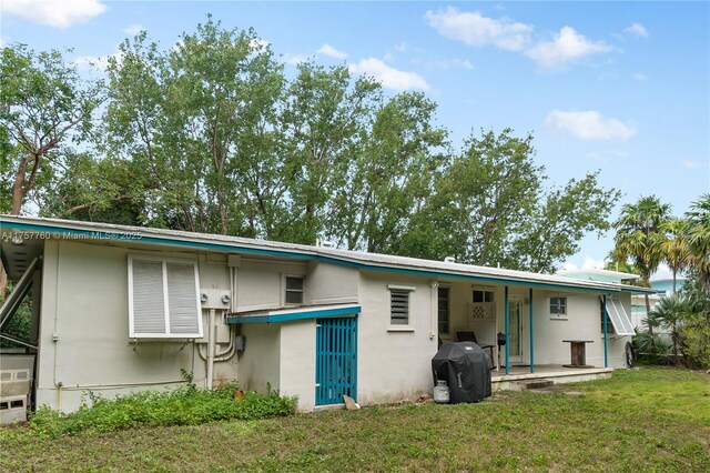 rear view of property featuring a patio, a lawn, and stucco siding