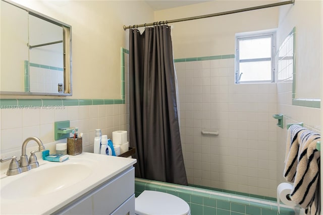 bathroom with wainscoting, toilet, tiled shower / bath, vanity, and tile walls