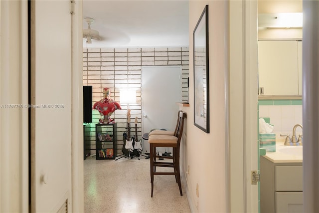 corridor with tile walls, a sink, and speckled floor