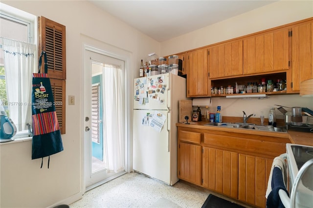 kitchen featuring light speckled floor, white appliances, a sink, open shelves, and brown cabinetry