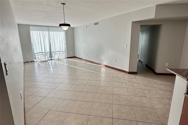 empty room featuring baseboards, visible vents, a textured ceiling, and light tile patterned flooring