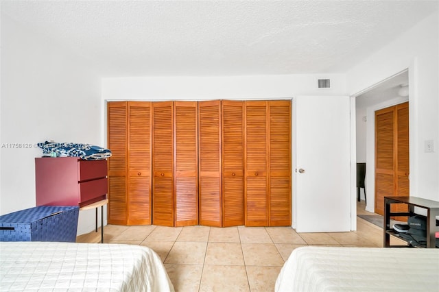 bedroom with a closet, visible vents, a textured ceiling, and light tile patterned floors