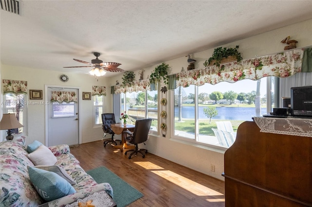 interior space featuring a ceiling fan, a textured ceiling, visible vents, and wood finished floors