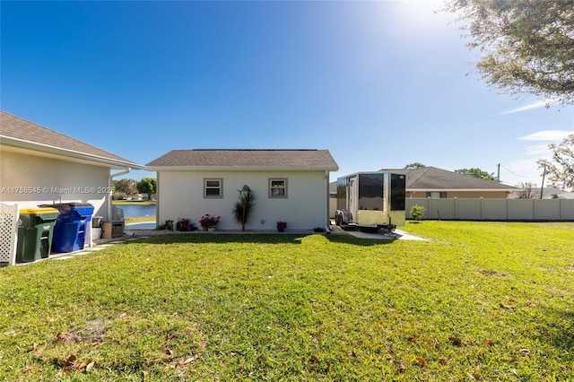 rear view of property featuring stucco siding, a water view, a lawn, fence, and an outdoor structure