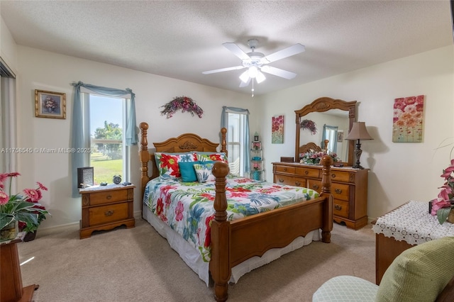 bedroom with ceiling fan, baseboards, a textured ceiling, and light colored carpet