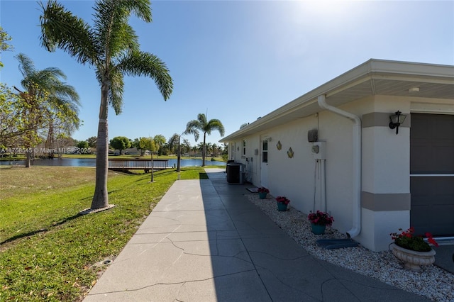 view of home's exterior featuring a yard, stucco siding, a water view, central AC, and a garage