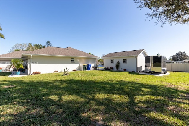 back of house with stucco siding, a yard, and fence