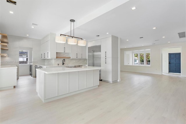 kitchen with built in refrigerator, light countertops, light wood-type flooring, backsplash, and a center island