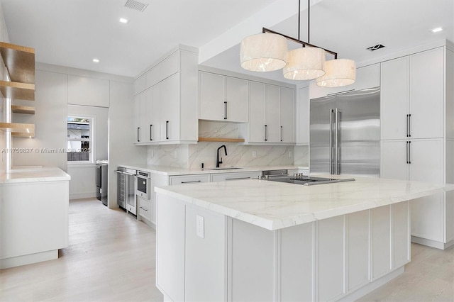 kitchen with light wood-style flooring, a sink, light stone countertops, backsplash, and built in fridge