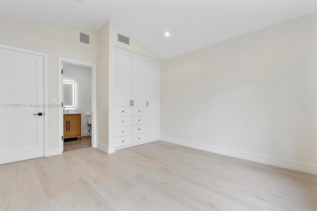 unfurnished bedroom with vaulted ceiling, light wood-type flooring, connected bathroom, and visible vents