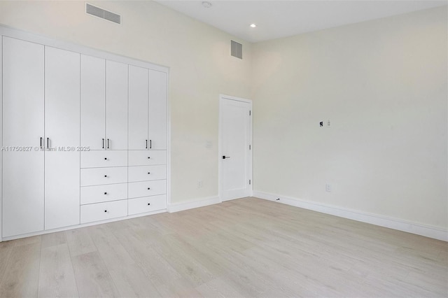 unfurnished bedroom with a high ceiling, baseboards, visible vents, and light wood finished floors