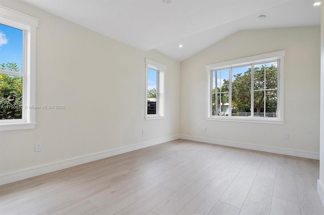 spare room featuring a healthy amount of sunlight, light wood finished floors, baseboards, and vaulted ceiling