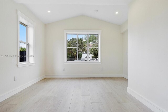 empty room featuring light wood-type flooring, plenty of natural light, lofted ceiling, and baseboards