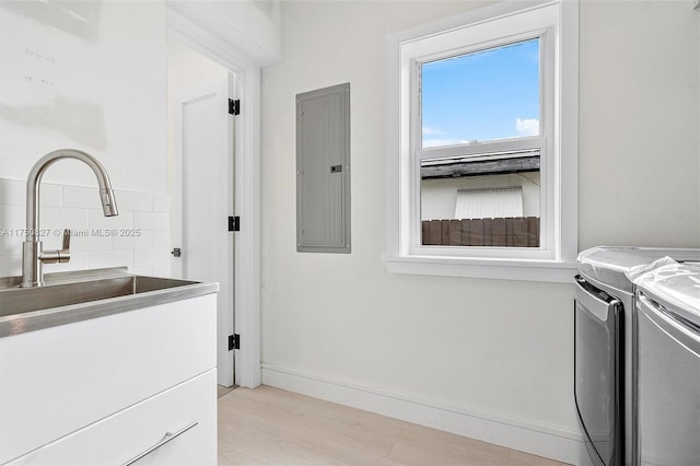 washroom featuring light wood-style flooring, washing machine and dryer, laundry area, electric panel, and baseboards