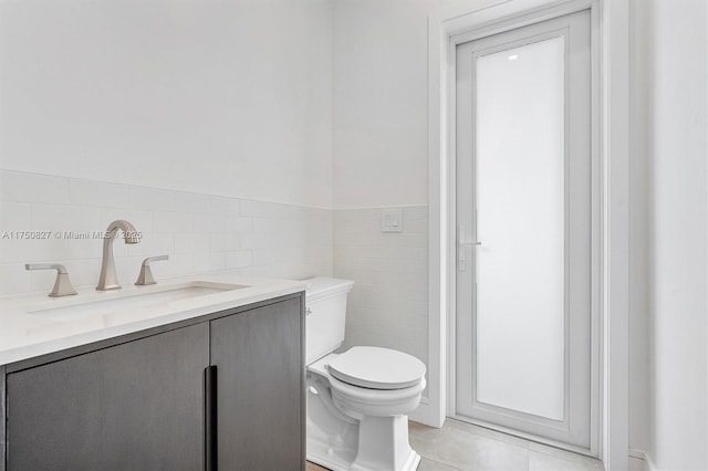 bathroom featuring a wainscoted wall, tile walls, toilet, vanity, and tile patterned flooring