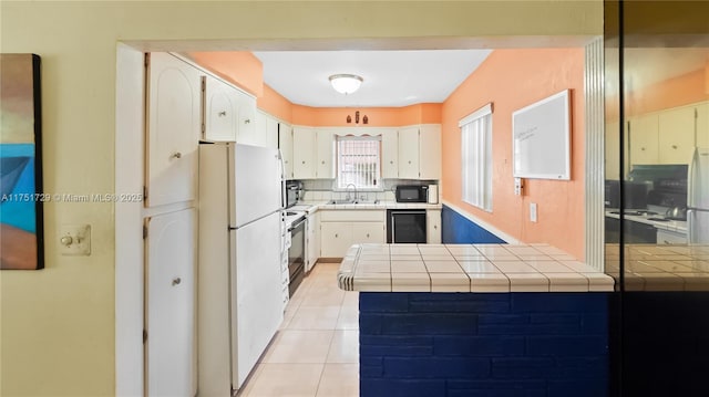 kitchen featuring black microwave, light tile patterned floors, a peninsula, tile counters, and freestanding refrigerator