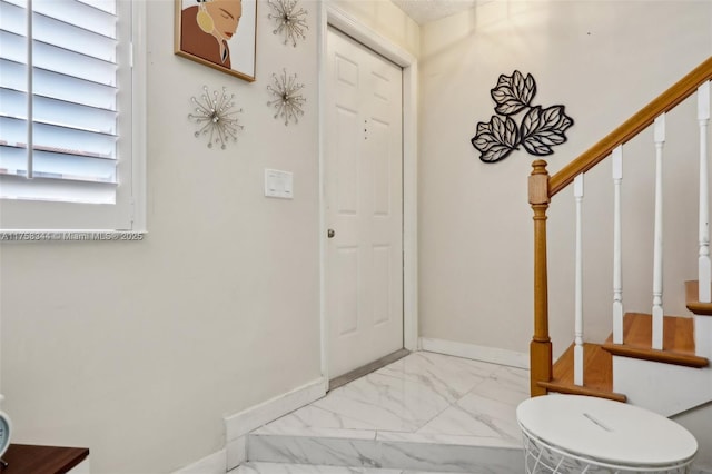 foyer with marble finish floor, stairway, and baseboards