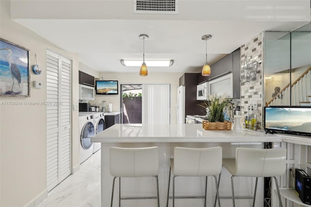 kitchen featuring marble finish floor, visible vents, white microwave, separate washer and dryer, and a peninsula