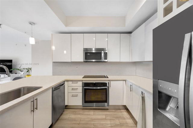 kitchen with appliances with stainless steel finishes, white cabinetry, light countertops, and a sink