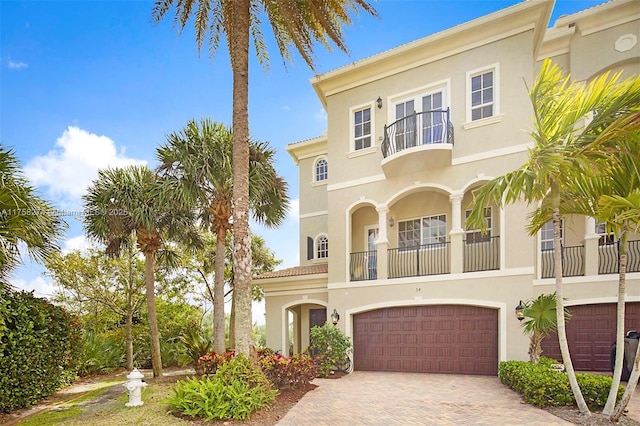 view of front facade featuring an attached garage, a balcony, decorative driveway, and stucco siding