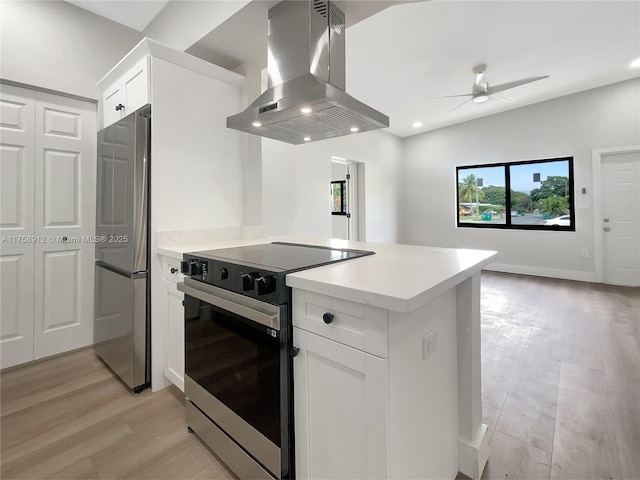 kitchen featuring range hood, black / electric stove, a peninsula, freestanding refrigerator, and light countertops