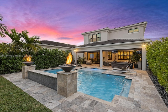 rear view of property featuring a patio area, stucco siding, an outdoor pool, and an outdoor living space with a fire pit