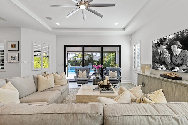 living area featuring baseboards, a raised ceiling, light wood-style flooring, and recessed lighting