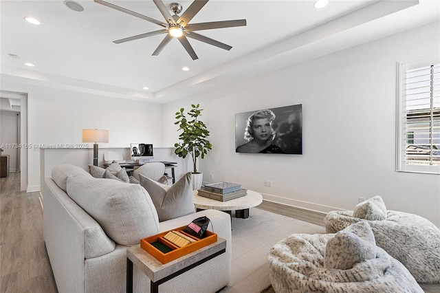 living area with recessed lighting, a raised ceiling, baseboards, and light wood finished floors