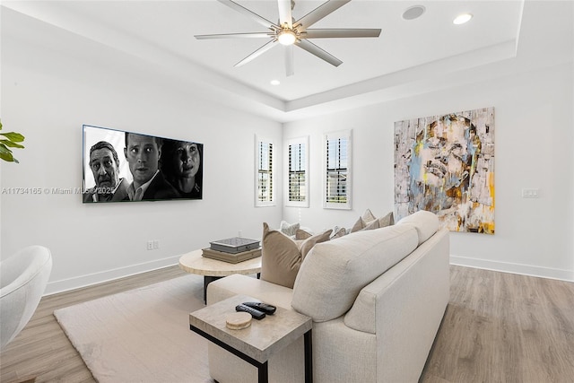 living room featuring light wood-type flooring, baseboards, and a raised ceiling