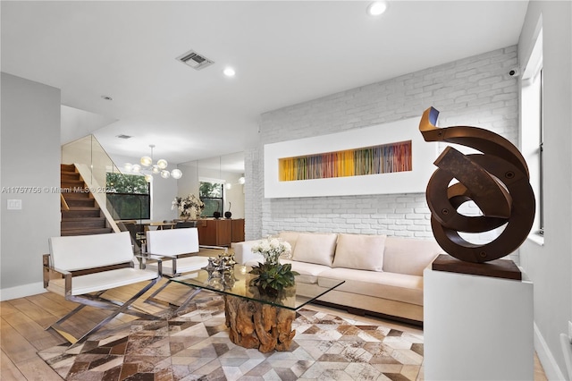 living area featuring wood finished floors, recessed lighting, stairway, an inviting chandelier, and brick wall