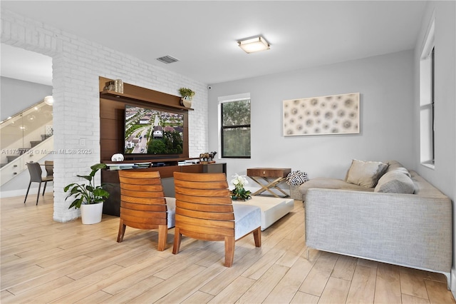 living room with stairway, visible vents, brick wall, and light wood finished floors