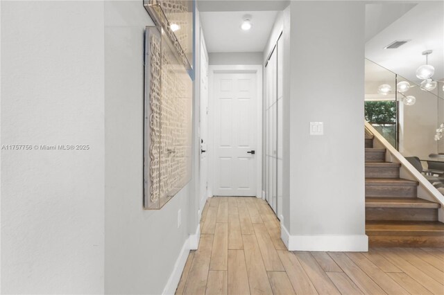 corridor featuring light wood finished floors, visible vents, baseboards, stairway, and a notable chandelier