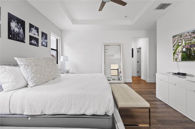 bedroom featuring visible vents, dark wood finished floors, baseboards, a raised ceiling, and ceiling fan