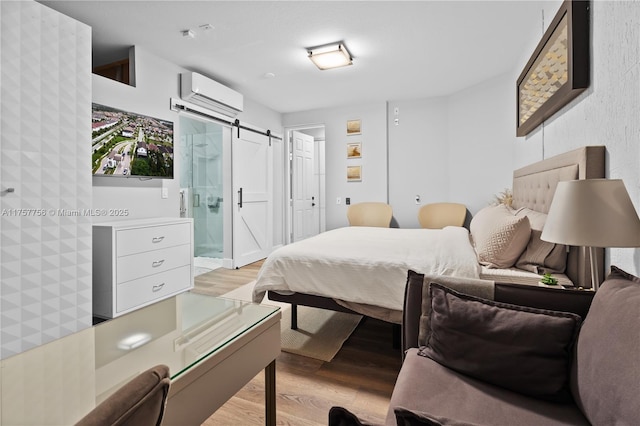 bedroom with a barn door, light wood finished floors, ensuite bathroom, and a wall unit AC