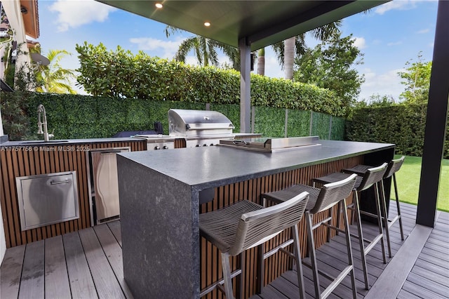 wooden terrace featuring grilling area, fence, outdoor wet bar, area for grilling, and a sink