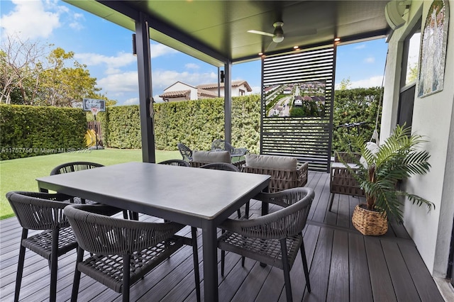 deck featuring outdoor dining area, a yard, a ceiling fan, and fence