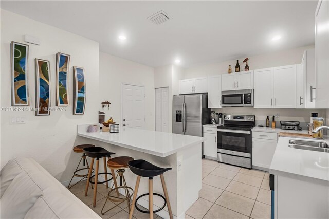 kitchen with light tile patterned flooring, a peninsula, a sink, a kitchen breakfast bar, and appliances with stainless steel finishes