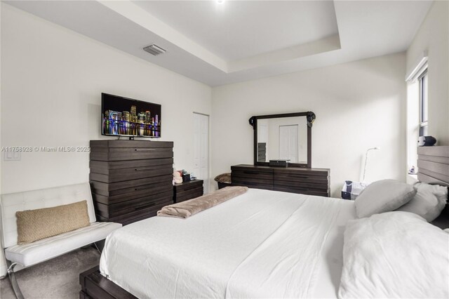 bedroom with a raised ceiling, visible vents, and carpet flooring