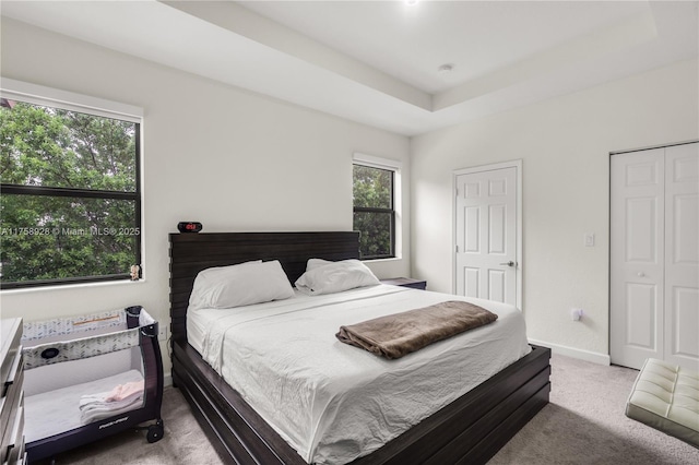 carpeted bedroom with a tray ceiling and baseboards